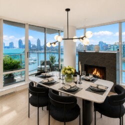 Modern dining room with a marble table for six, a contemporary chandelier, and a fireplace, overlooking a waterfront city skyline.