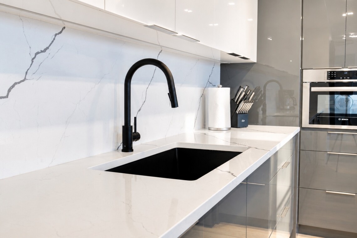 Modern kitchen with white marble counters, black curved faucet, and recessed sink area.