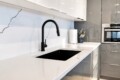 Modern kitchen with white marble counters, black curved faucet, and recessed sink area.