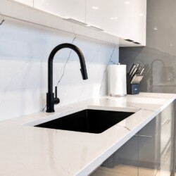 Modern kitchen with white marble counters, black curved faucet, and recessed sink area.