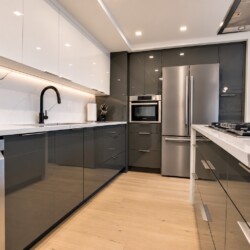 Modern kitchen with white upper cabinets, gray lower cabinets, black faucet, marble backsplash, and stainless steel appliances.