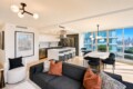 Open-concept living area with a white marble kitchen island, black sofa, and large windows overlooking a cityscape.