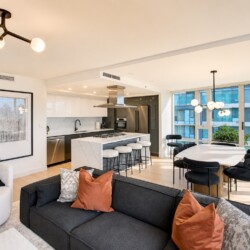 Open-concept living area with a white marble kitchen island, black sofa, and large windows overlooking a cityscape.