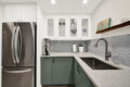 Modern kitchen with white upper cabinets, glass-front display cabinet, and gray hex tile backsplash over a light quartz countertop