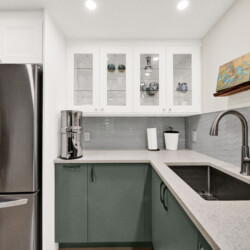 Modern kitchen with white upper cabinets, glass-front display cabinet, and gray hex tile backsplash over a light quartz countertop