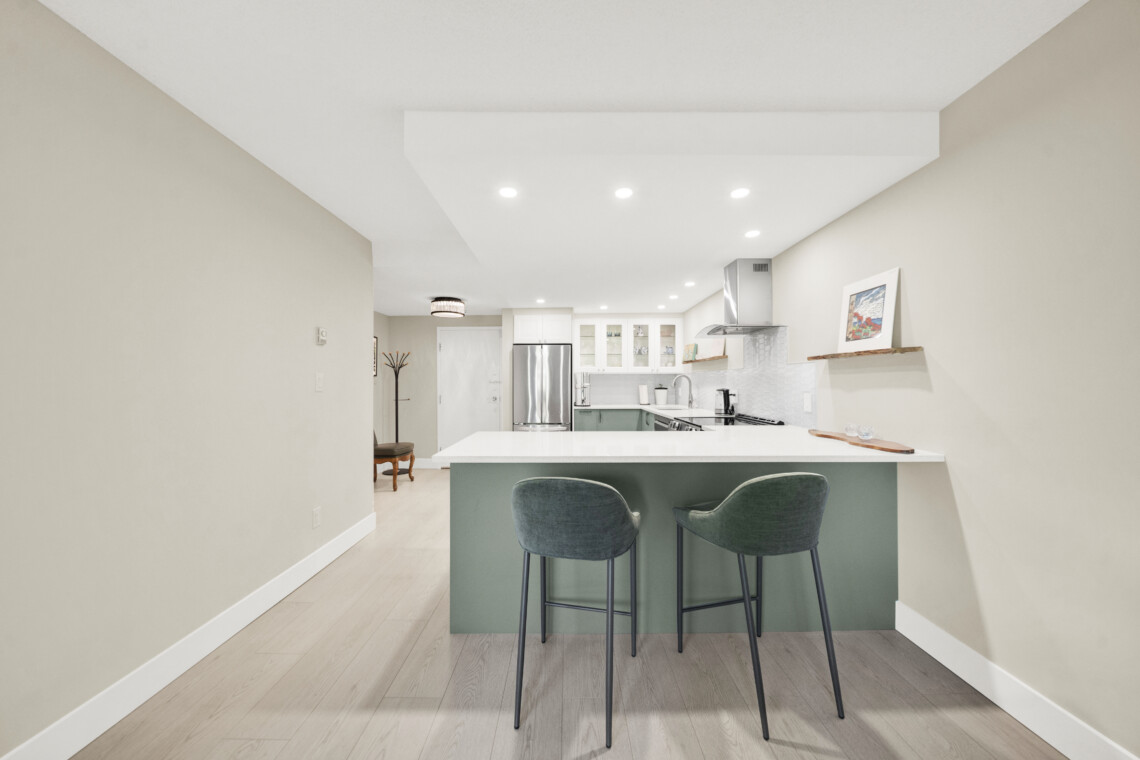 Modern kitchen with an island and three green bar stools facing the counter; light wood floor and beige walls.