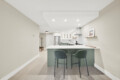 Modern kitchen with an island and three green bar stools facing the counter; light wood floor and beige walls.