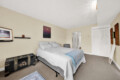 Bedroom with a queen bed, white quilt, blue throw, and two black decorative trunks at the foot of the bed on a beige wall.