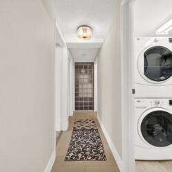 Narrow hallway with a stacked washer/dryer on the right, beige walls, and a patterned rug running down the floor.