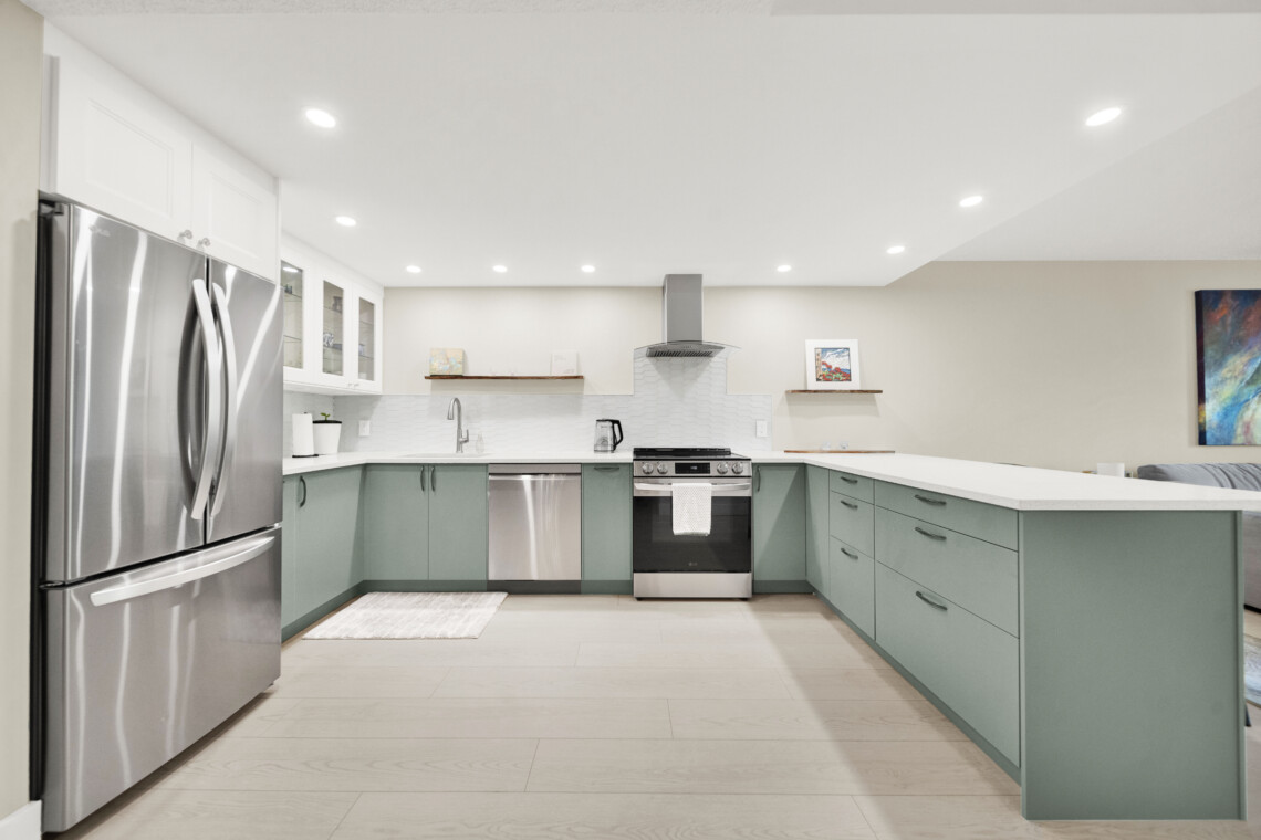 Modern kitchen with a stainless steel French-door fridge, white upper cabinets, and green lower cabinets surrounding a central stove area.