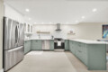 Modern kitchen with a stainless steel French-door fridge, white upper cabinets, and green lower cabinets surrounding a central stove area.