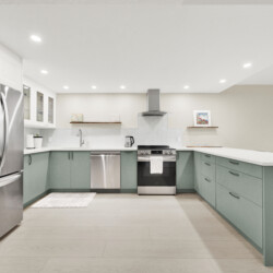 Modern kitchen with a stainless steel French-door fridge, white upper cabinets, and green lower cabinets surrounding a central stove area.