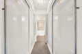 Narrow hallway with glass-front cabinets on both sides, reflecting light from ceiling chandeliers and leading to a lit room at the end.