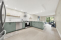 Bright modern kitchen with green lower cabinets, stainless steel appliances, and white tile backsplash; open to a living area with a large window.