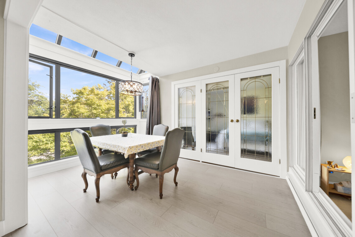 Bright dining room with large windows and skylights, letting in lots of natural light; a table with a yellow floral tablecloth and upholstered chairs around it.