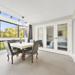 Bright dining room with large windows and skylights, letting in lots of natural light; a table with a yellow floral tablecloth and upholstered chairs around it.