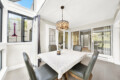 Sunlit indoor dining area with a daisies-pattern tablecloth, glass doors, and a decorative chandelier.