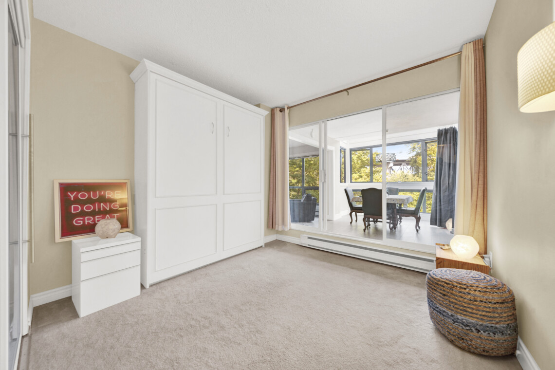 Bright living room with a white built-in wardrobe, beige walls, and a large window with pink curtains.
