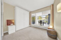Bright living room with a white built-in wardrobe, beige walls, and a large window with pink curtains.