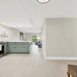 Modern kitchen with mint-green cabinets, stainless steel stove and range hood, and a white tile backsplash; living room visible in the background.