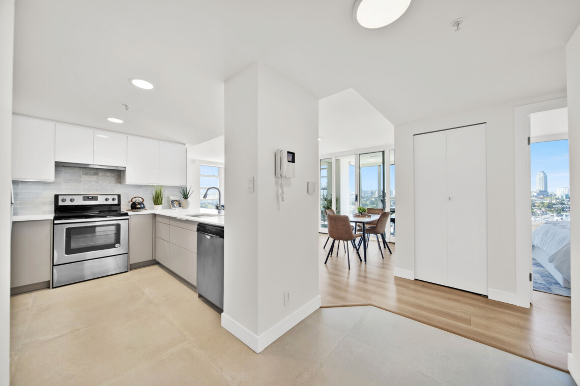 Bright open kitchen with white cabinets and stainless steel stove, adjacent dining area with city view.