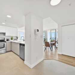 Bright open kitchen with white cabinets and stainless steel stove, adjacent dining area with city view.