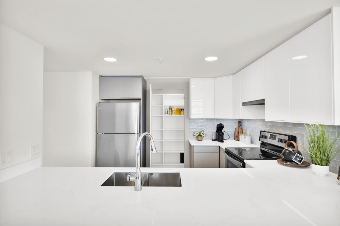 Bright, modern kitchen with white cabinets, a stainless steel refrigerator, and an island sink in a sunlit space.