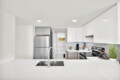 Bright, modern kitchen with white cabinets, a stainless steel refrigerator, and an island sink in a sunlit space.