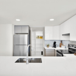 Bright, modern kitchen with white cabinets, a stainless steel refrigerator, and an island sink in a sunlit space.