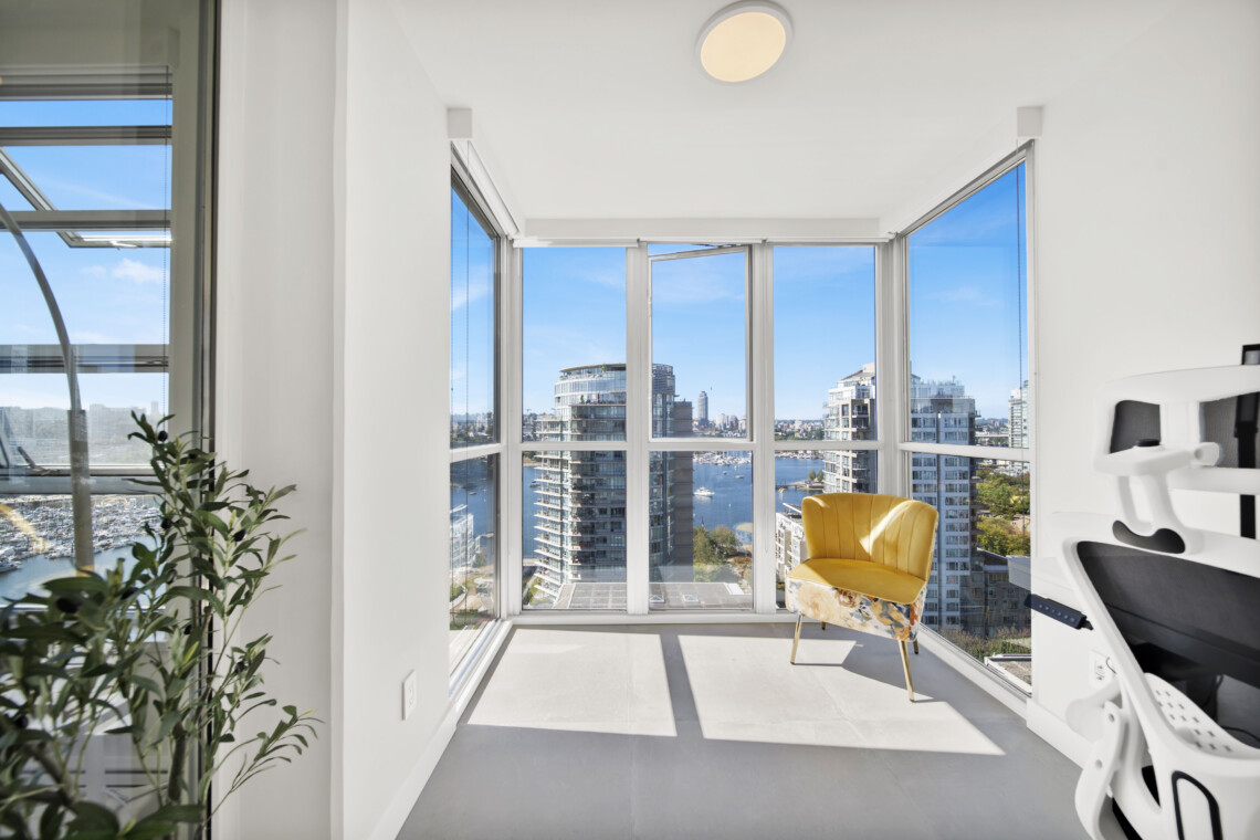 Bright, modern treatment room with floor-to-ceiling windows showing a city harbor and a yellow chair by the wall-mounted equipment.
