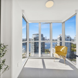 Bright, modern treatment room with floor-to-ceiling windows showing a city harbor and a yellow chair by the wall-mounted equipment.