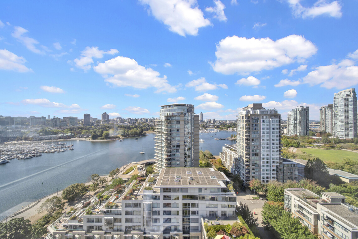 City skyline with modern high-rise buildings along a marina under a blue sky with scattered clouds.