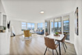 Bright modern living room with white walls, large windows, and a seating area overlooking a cityscape outside the windows.
