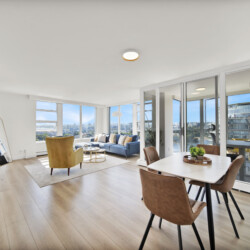 Bright modern living room with white walls, large windows, and a seating area overlooking a cityscape outside the windows.