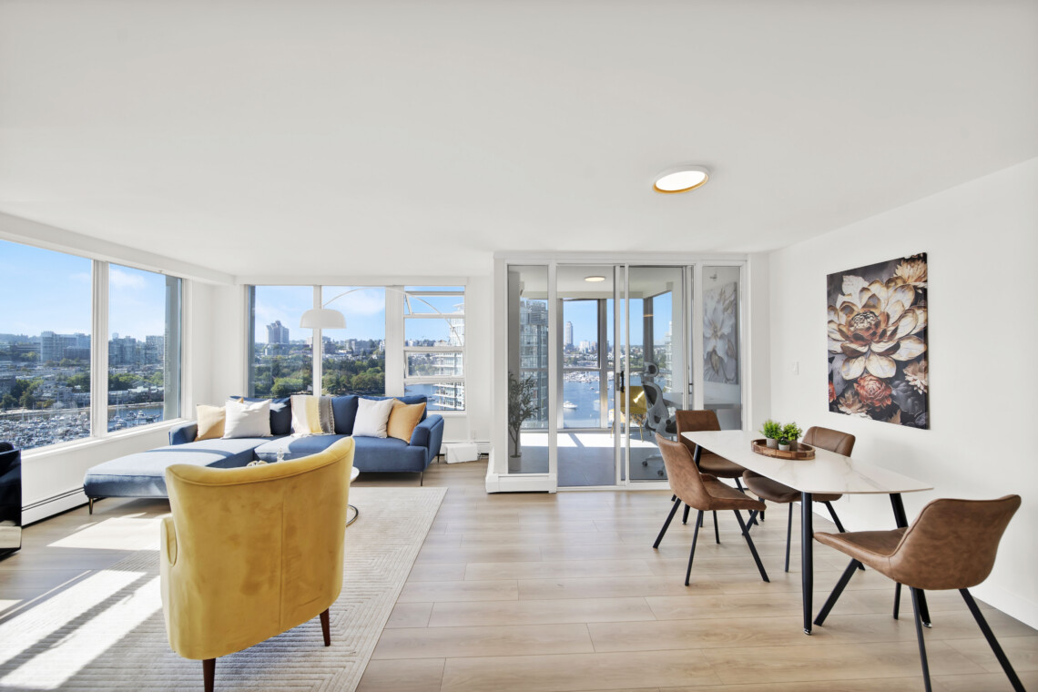 Bright, open living room with large windows showing a city skyline, blue sofa and mustard chairs.