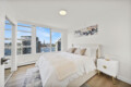 Bright modern bedroom with a large window view of a cityscape and water, white bed and beige throw pillows.