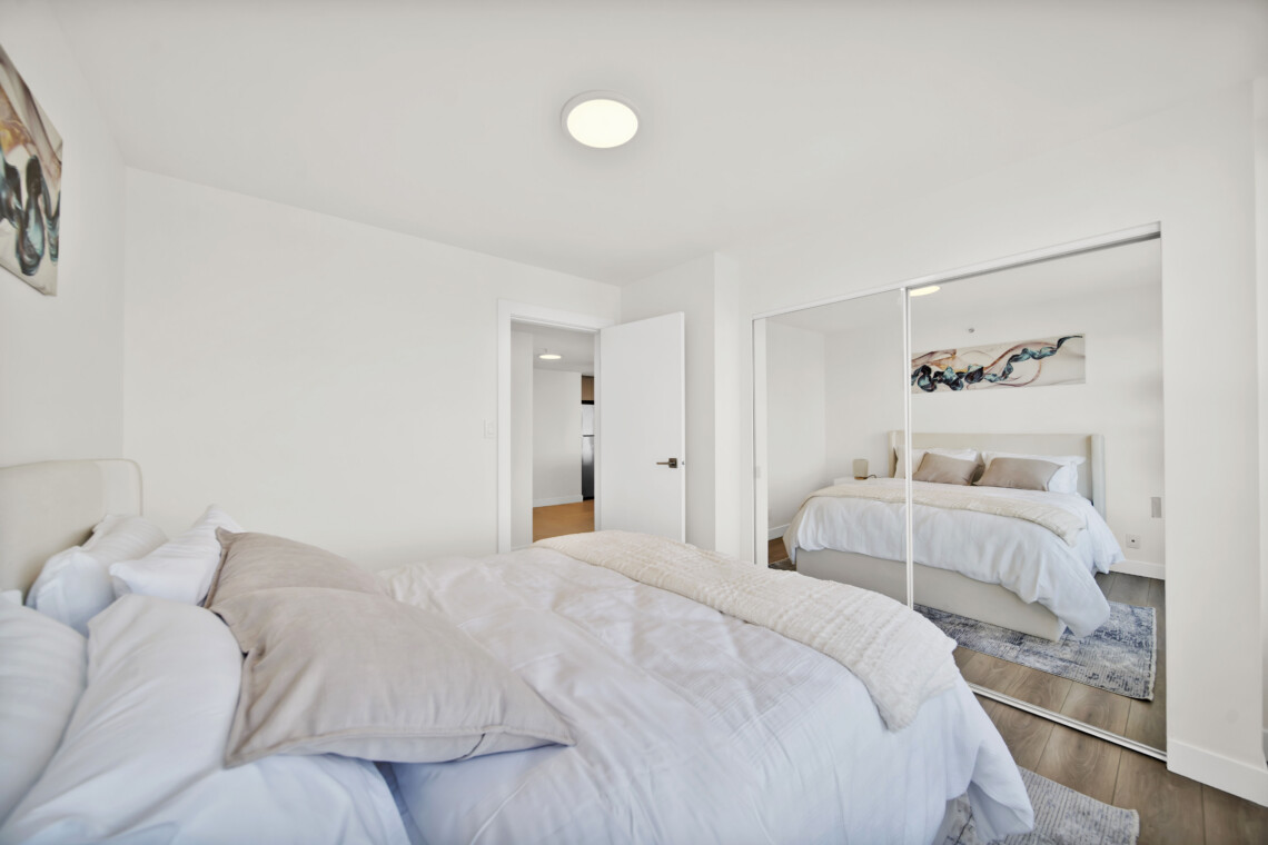 Bright minimalist bedroom with two white beds, a mirrored wardrobe, and white walls reflecting light.