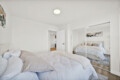 Bright minimalist bedroom with two white beds, a mirrored wardrobe, and white walls reflecting light.