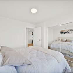 Bright minimalist bedroom with two white beds, a mirrored wardrobe, and white walls reflecting light.