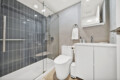 Modern bathroom showing a glass-enclosed shower with dark gray tile, white toilet, and white vanity with sink fixtures.