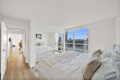 Bright, minimalist bedroom with large windows and a river/city view. The room has two beds and white bedding.