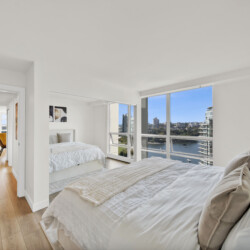 Bright, minimalist bedroom with large windows and a river/city view. The room has two beds and white bedding.