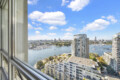 View from a window over a marina cityscape with boats and modern high-rise buildings against a blue sky with clouds.