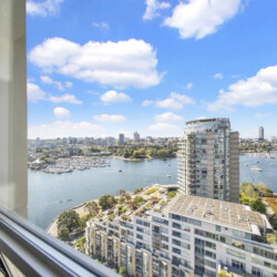 View from a window over a marina cityscape with boats and modern high-rise buildings against a blue sky with clouds.