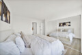 Bright modern bedroom with two white-duvet beds, beige pillows, and a mirrored wardrobe reflecting the room.
