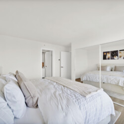 Bright modern bedroom with two white-duvet beds, beige pillows, and a mirrored wardrobe reflecting the room.