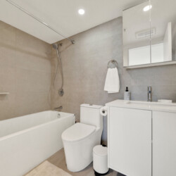 Modern bathroom with a bathtub, handheld shower, beige tiling, and a white vanity with mirrored cabinet above it.