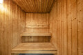 Wood-paneled sauna interior with two-tier wooden benches along the back wall and warm lighting.