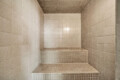 Empty tiled shower alcove with a three-tier built-in bench, beige square tiles everywhere