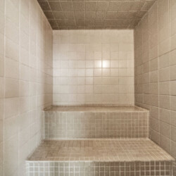 Empty tiled shower alcove with a three-tier built-in bench, beige square tiles everywhere
